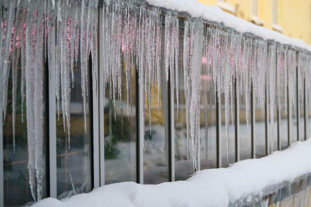 Frozen icicles hanging from roof on glasshouse. Snow melting during early spring and snowbreak