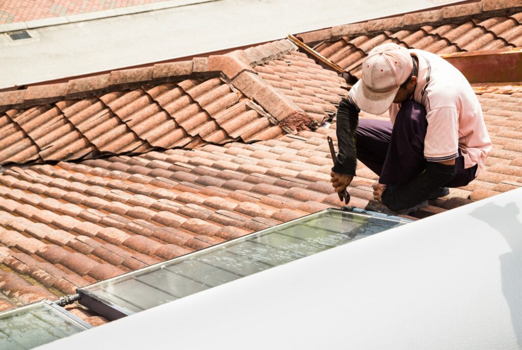 Worker fixing solar water heater on roof during maintenance